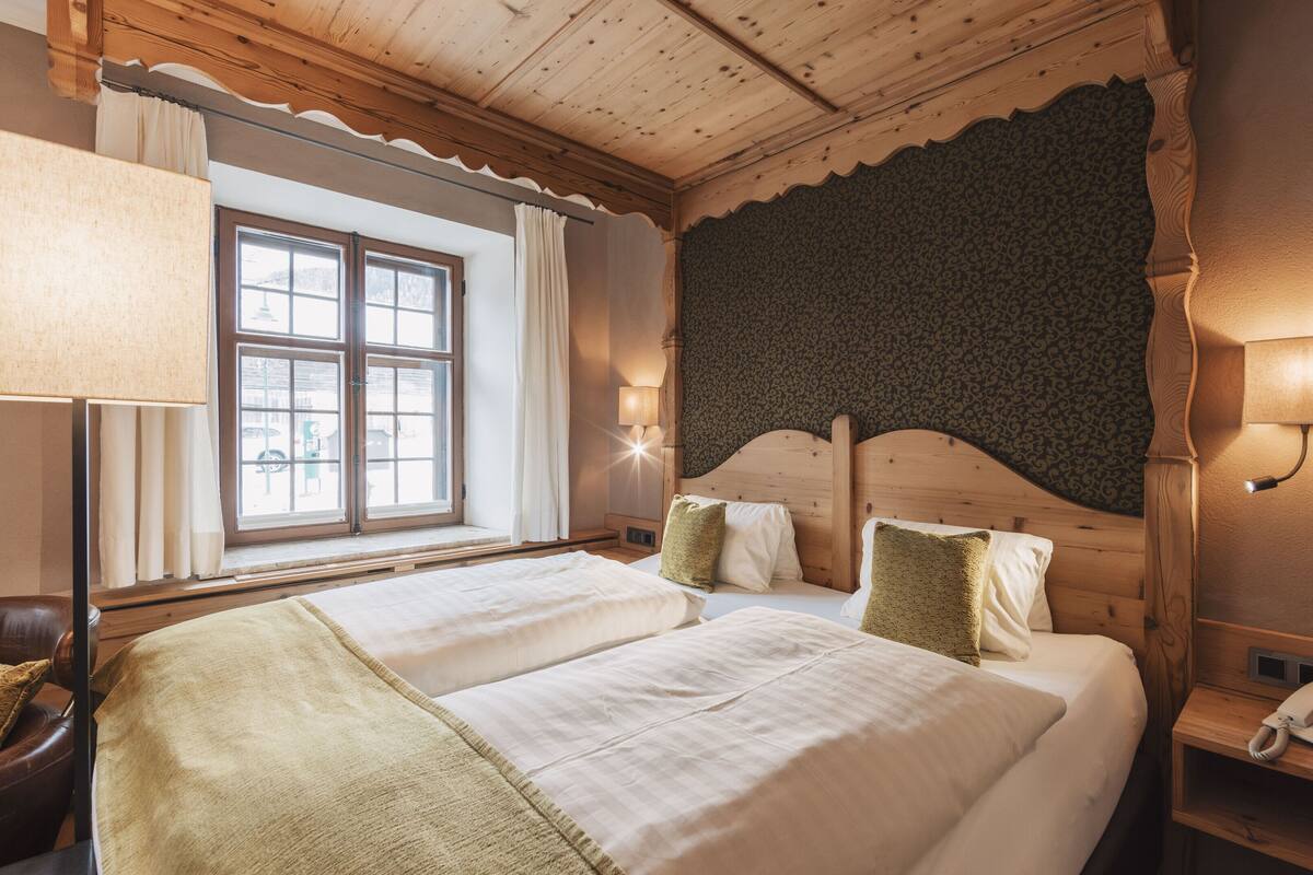 Habitación de hotel con dos camas, una ventana con cortinas, una lámpara, un teléfono y una pared con estampado.