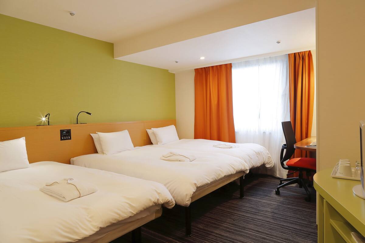 A hotel room with two beds, a desk, and a chair.