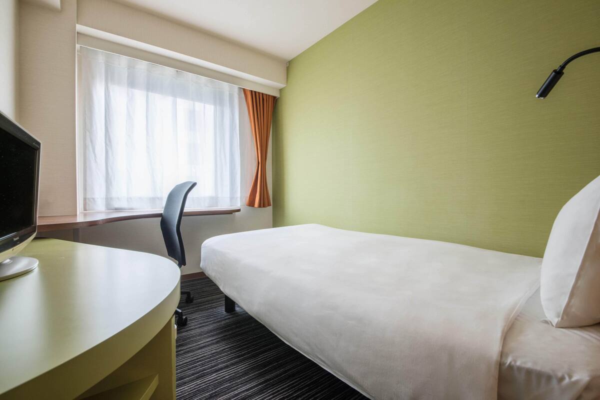 A hotel room with a bed, a desk with a computer, and a window with curtains.