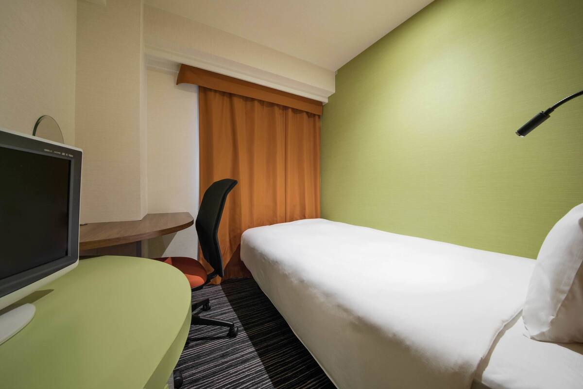 A hotel room with a single bed, a desk with a computer, and a chair.