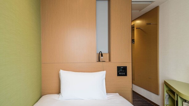 Une chambre d’hôtel avec une tête de lit en bois, un lit avec une literie blanche, un panneau de commande et un miroir.