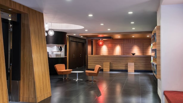 A modern reception area with a wooden reception desk, two orange chairs, a small table, and a red spherical light fixture. - the b ikebukuro (Tokyo)