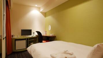 Quarto de hotel com cama, escrivaninha com computador, cadeira, pequeno frigorífico e janela com cortinas.
