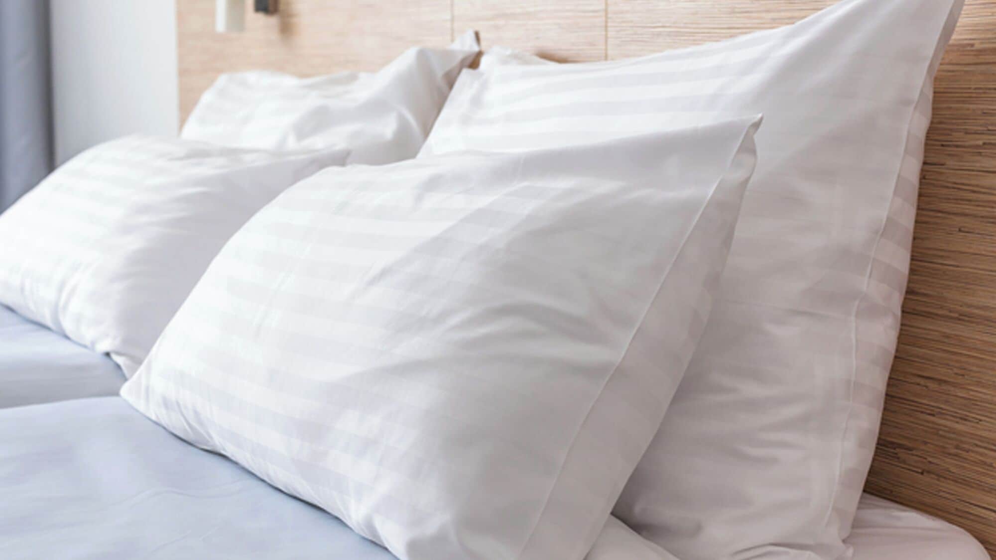 A bed with white bedding and pillows, a wooden headboard, and a light-colored wall.