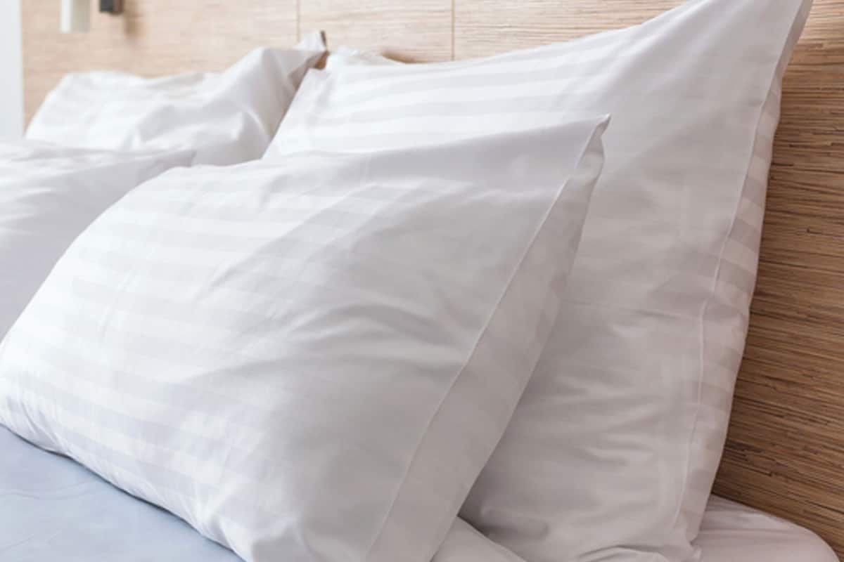 A bed with white bedding and pillows, a wooden headboard, and a light-colored wall.