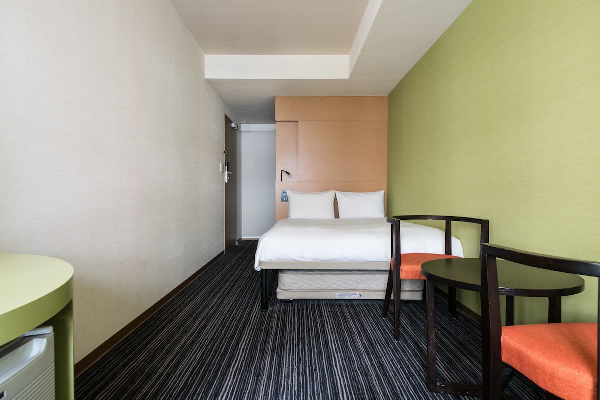 A hotel room with a bed, a small table, and a chair.