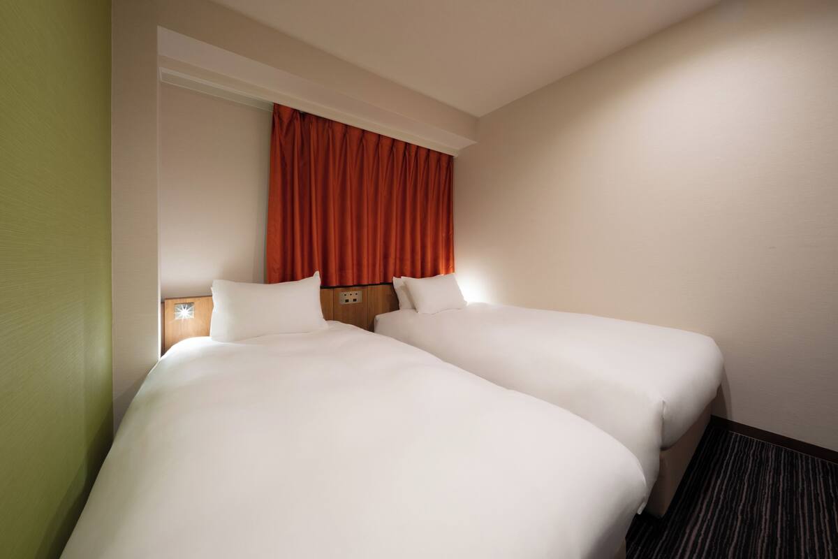 A hotel room with two beds, a wooden headboard, a red curtain, and a carpeted floor.