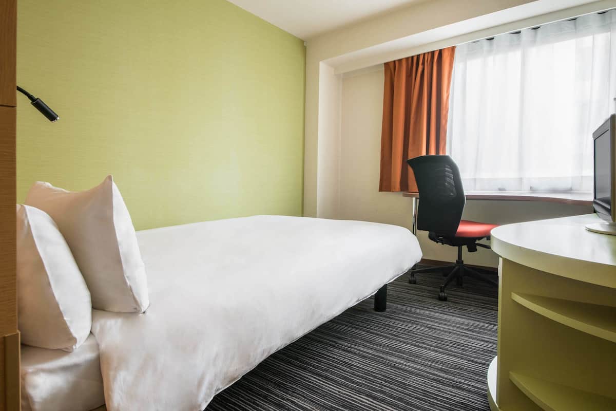 A hotel room with a bed, a desk, a chair, and a television.