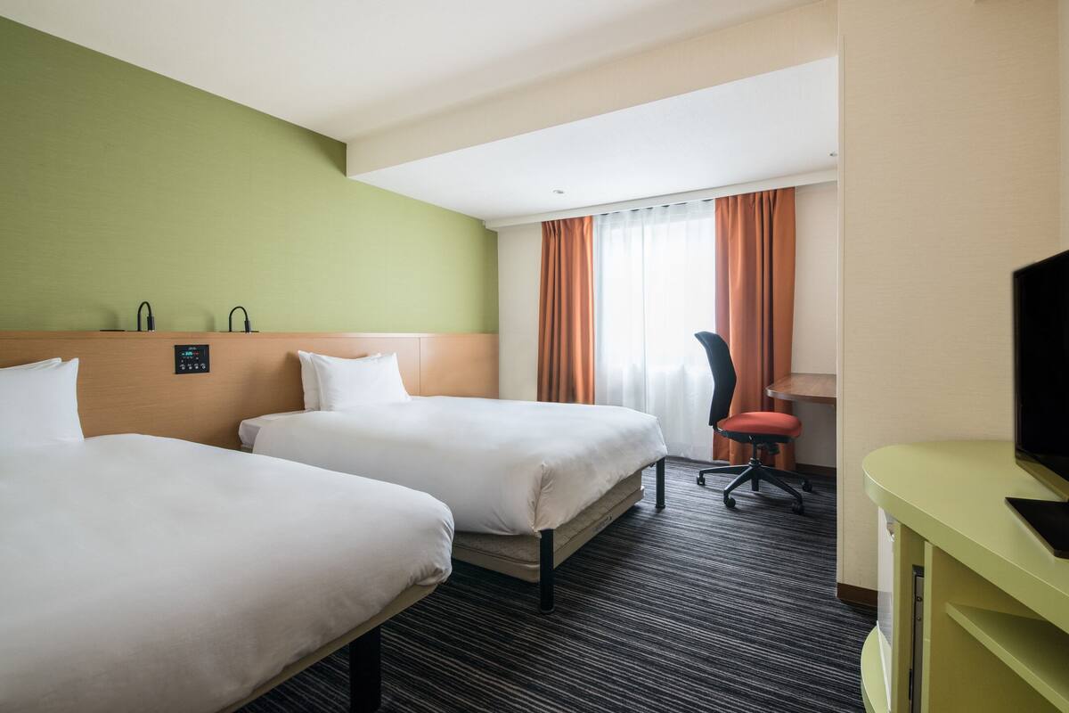 A hotel room with two beds, a desk, a chair, and a television.