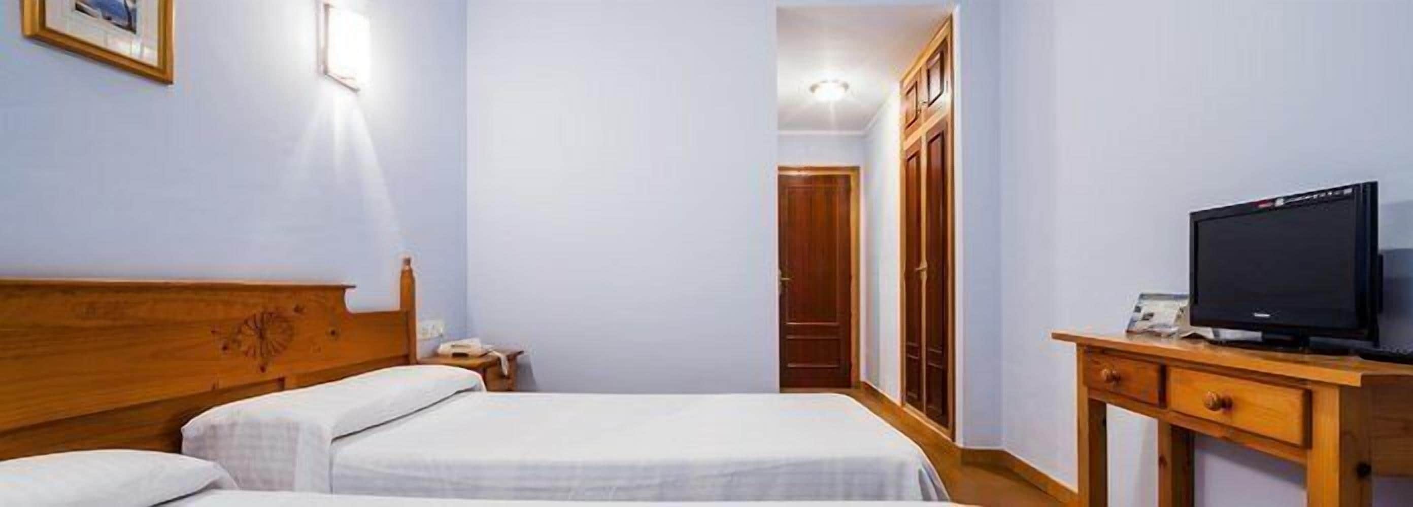 Een hotelkamer met een bed, een televisie op een houten standaard en een kledingkast.