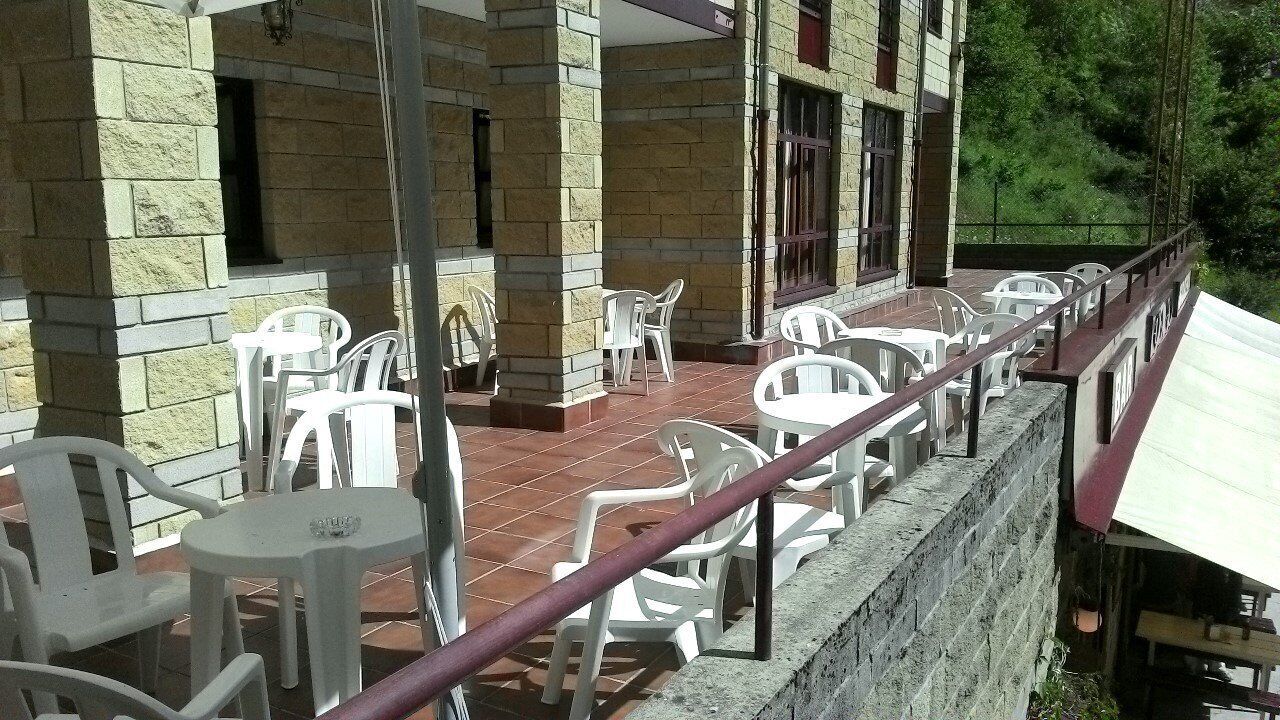 A covered outdoor area with white plastic chairs and tables, stone walls, and a railing.