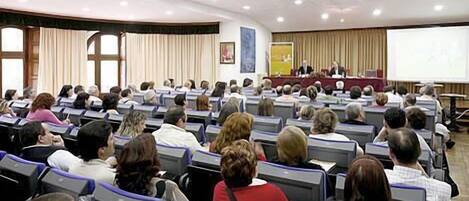 Un salón de conferencias con filas de sillas orientadas hacia un escenario con un atril y una pantalla.