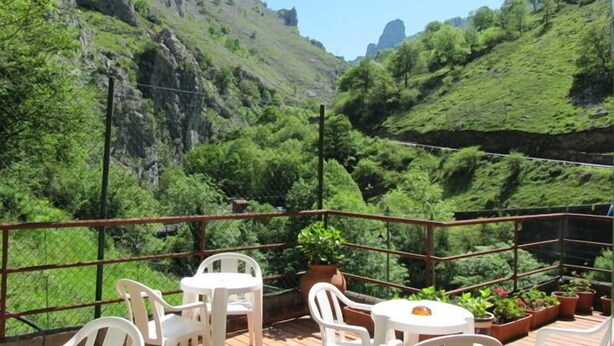 A terrace with white plastic chairs and tables, overlooking a lush valley with mountains in the background. - Arcea Hotel Mirador de Cabrales (Cabrales)