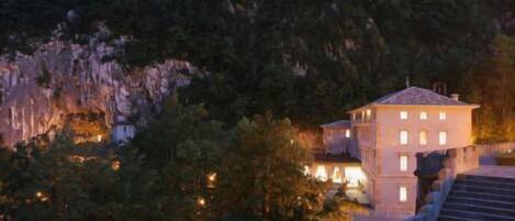 A building with multiple windows, surrounded by trees and a rocky landscape.