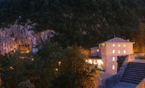 A building with multiple windows, surrounded by trees and a rocky landscape.