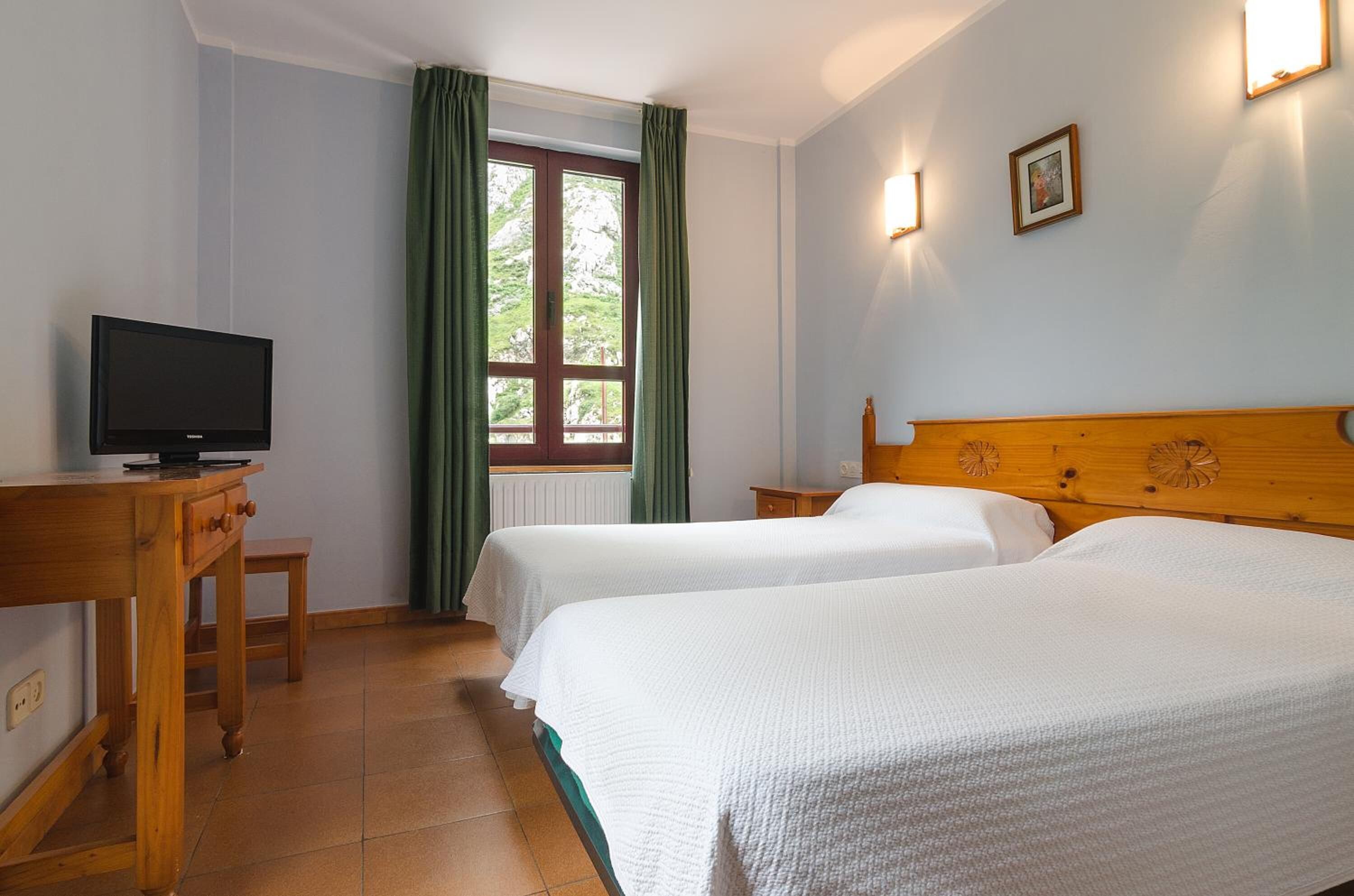 A hotel room with two beds, a wooden headboard, a television on a desk, and a window with curtains.