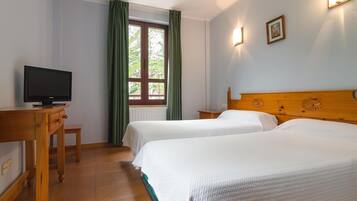A hotel room with two beds, a wooden headboard, a television on a desk, and a window with curtains.