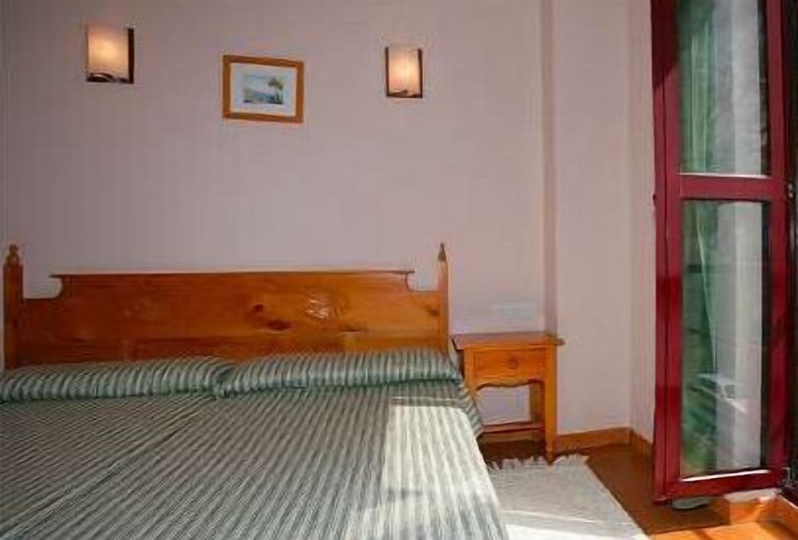 Un dormitorio con una cama de madera, una mesita de noche y una ventana con marco rojo.