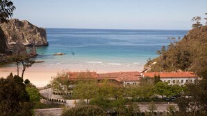 Une vue côtière comprenant une plage, des falaises rocheuses et des bâtiments aux toits recouverts de tuiles rouges.