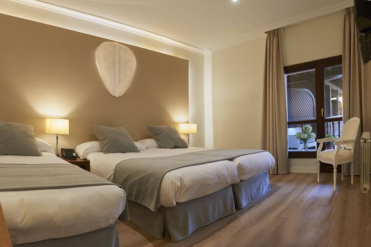 Habitación de hotel con dos camas, un escritorio, una silla, una lámpara y una ventana con cortinas.