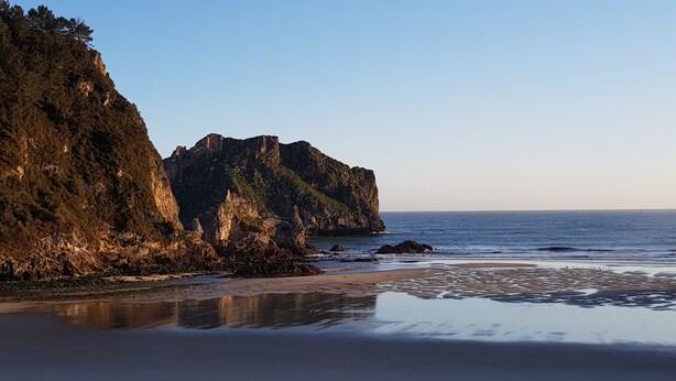 Une plage bordée de falaises rocheuses et aux eaux calmes.