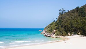 Uma praia com águas turquesa cristalinas, areia dourada e um morro coberto de árvores.