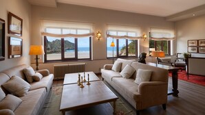 Uma sala de estar ampla com uma grande janela com vista para a praia, mobiliada com sofá, mesa de centro e luminárias.