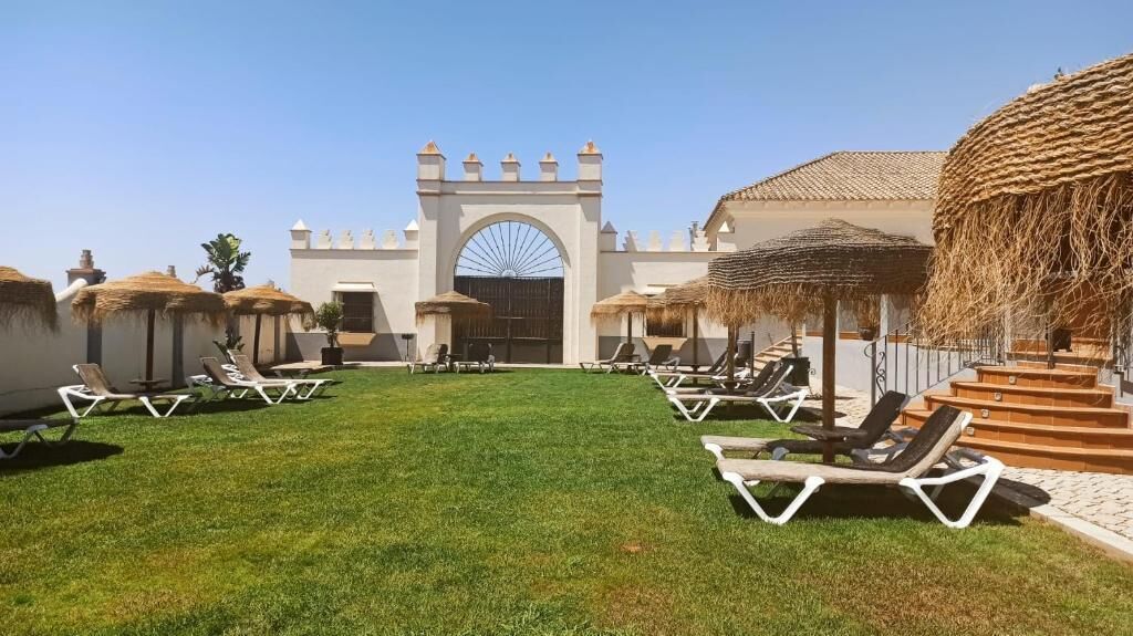A courtyard with a white building, a large arched entrance, and lounge chairs.