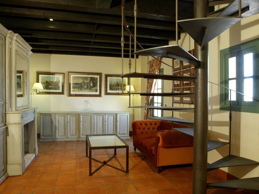 A room with a fireplace, a sofa, a table, and a spiral staircase.