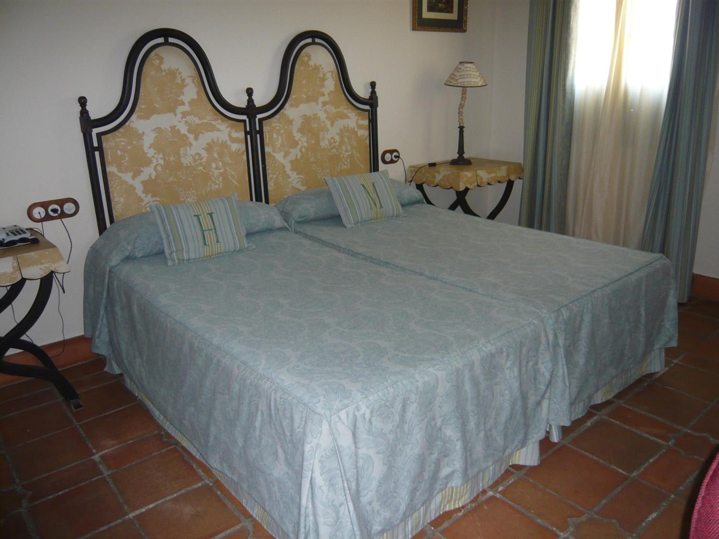 A bed with a headboard, a bedside table with a lamp, and a wall-mounted telephone.