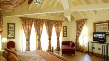 A hotel room with a large bed, a red armchair, a television, and patterned curtains.