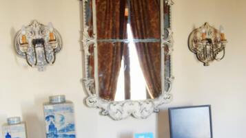 A room with a desk, two red chairs, a computer, a decorative mirror, and wall sconces.