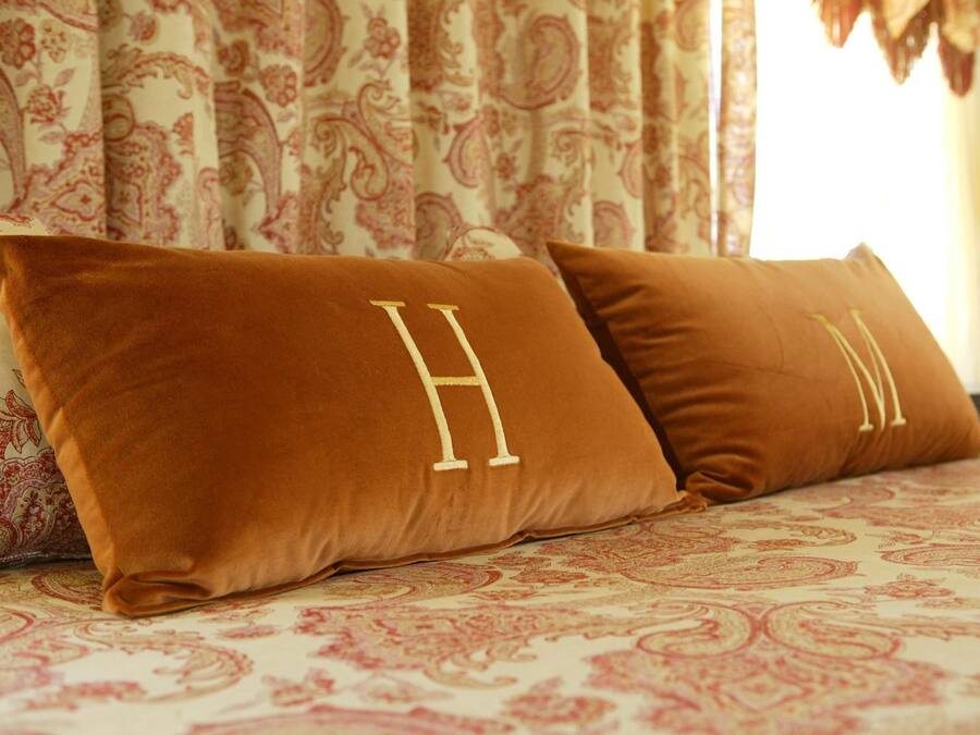 Een bed met een gebedruid sprei en twee bruine kussens met geborduurde letters.