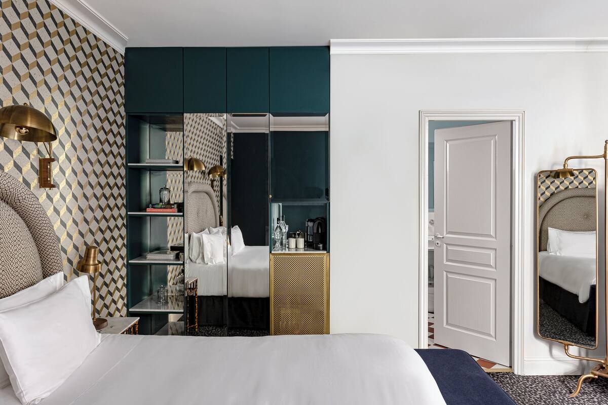 A hotel room with a bed, bedside table, lamp, wardrobe, and a mirror.