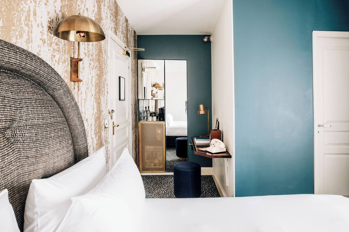 A hotel room with a bed, a desk, a mirror, and a wardrobe.