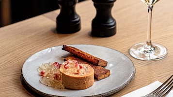 Una mesa de madera con un plato de comida, una copa de vino blanco y un molinillo de pimienta.