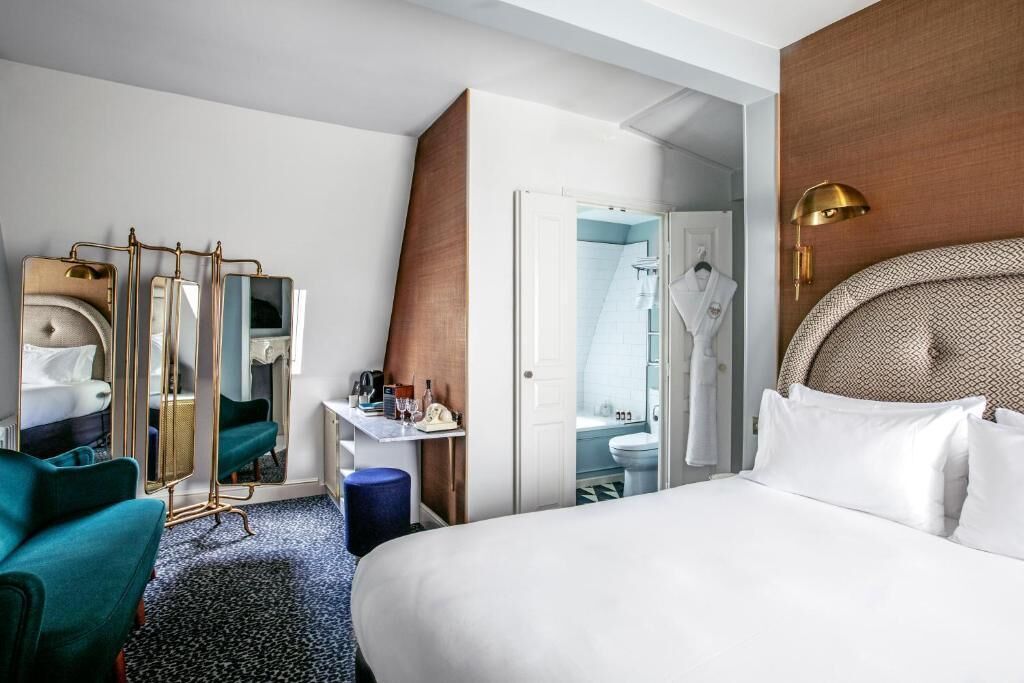 A hotel room with a large bed, a desk with a mirror, a chair, and a bathroom visible through an open door.