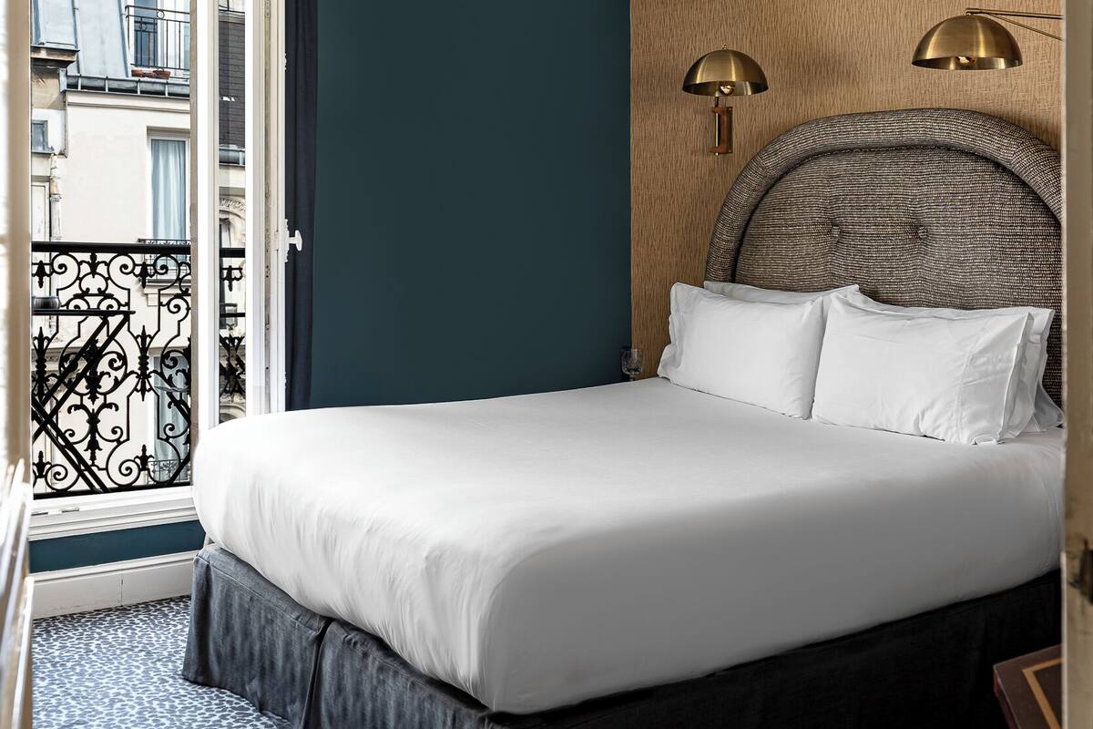 A hotel room with a large bed, a balcony with a wrought iron railing, and a view of the city.