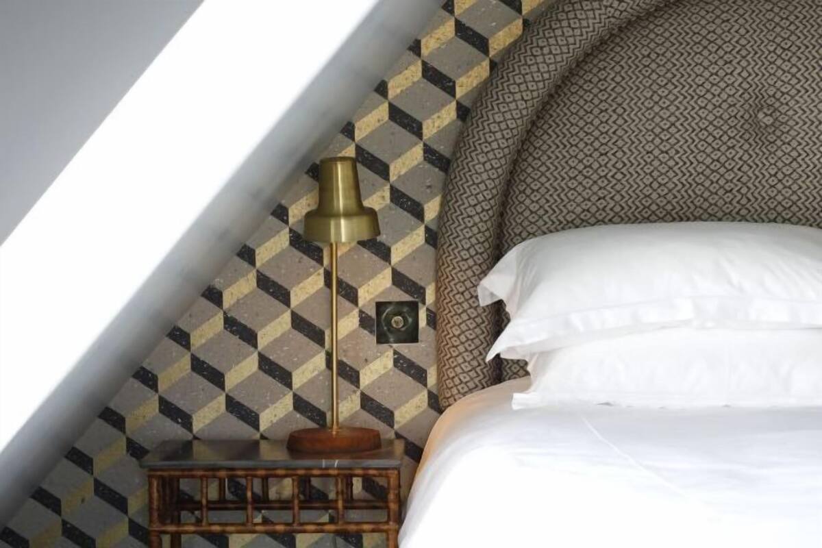 A bedroom with a checkered wall pattern, a bed with white bedding, and a bedside table with a lamp.