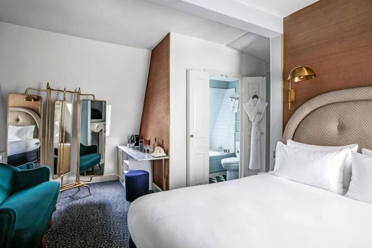 A hotel room with a bed, a desk, a mirror, a wardrobe, and a bathroom visible through an open door.