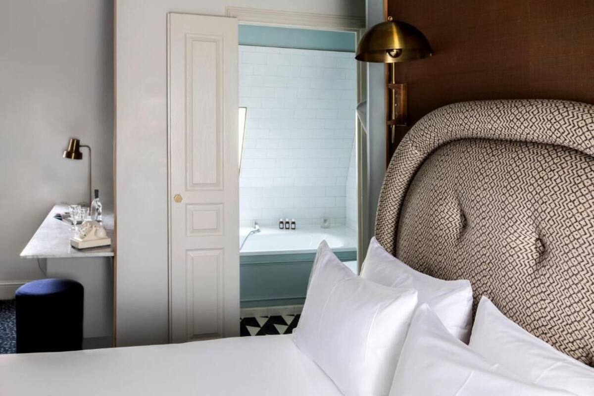 A hotel room with a bed, a desk, and a bathroom visible through an open door.
