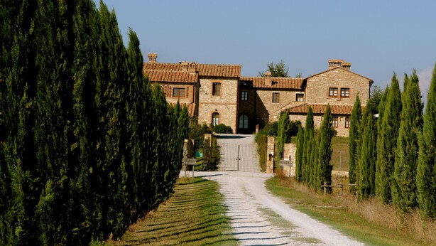A stone building with a tiled roof, surrounded by tall cypress trees and a gravel path leading to the entrance. - Borgo Beccanella (Asciano)
