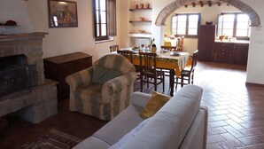 A cozy living room with a fireplace, a dining area with a table set for four, and an arched doorway leading to a kitchen. - Borgo Beccanella (Asciano)