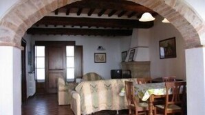 A dining area with a rustic stone archway, wooden furniture, and tiled flooring. - Borgo Beccanella (Asciano)
