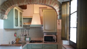 A kitchen with green cabinets, a brick archway, a microwave, and a stove. - Borgo Beccanella (Asciano)