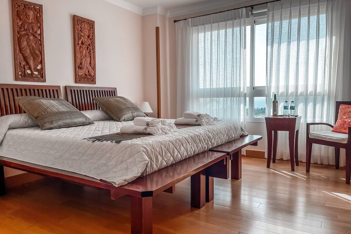 Een goed verlichte slaapkamer met een groot bed, een houten hoofdbord en twee decoratieve panelen aan de muur.
