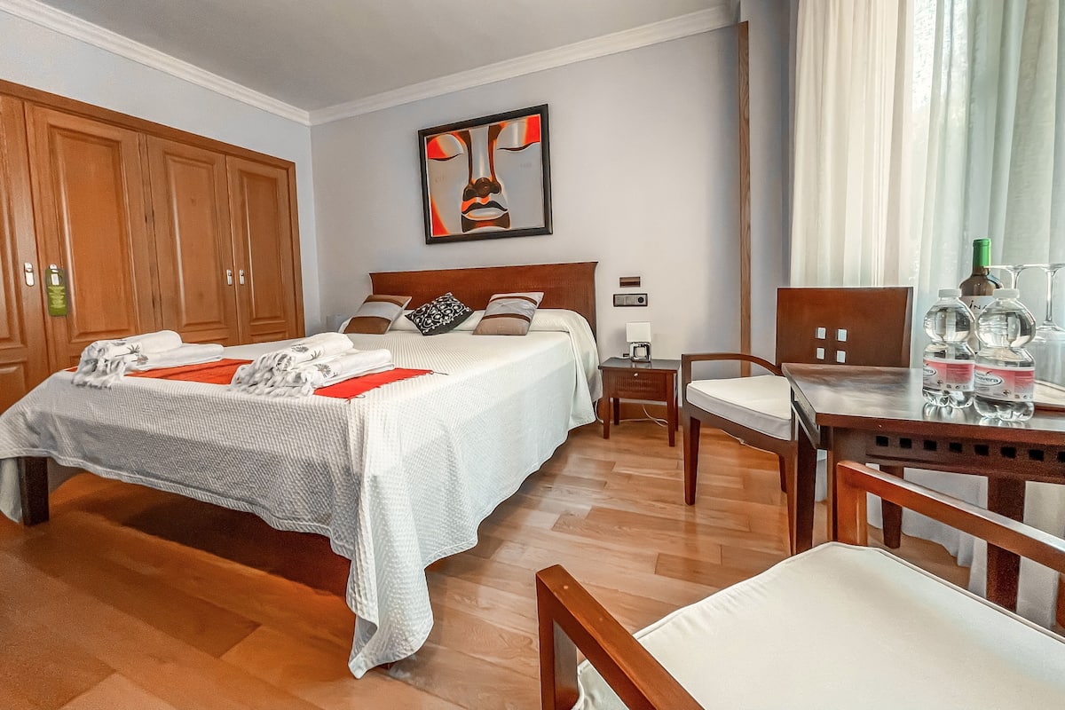 Een hotelkamer met een groot bed, een houten garderobe, een bureau met stoel en een schilderij aan de muur.