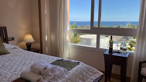 A hotel room with a bed, a nightstand, a lamp, a table with a bottle and glasses, and a view of the ocean. - The Marbella Heights Boutique Hotel (Marbella)