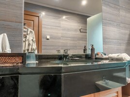 A modern bathroom with a large mirror, a black countertop, and a wooden door.