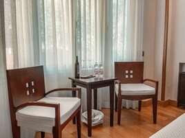 Una habitación con dos sillas de madera, una mesita con una botella y vasos, y una cama con colchón blanco.